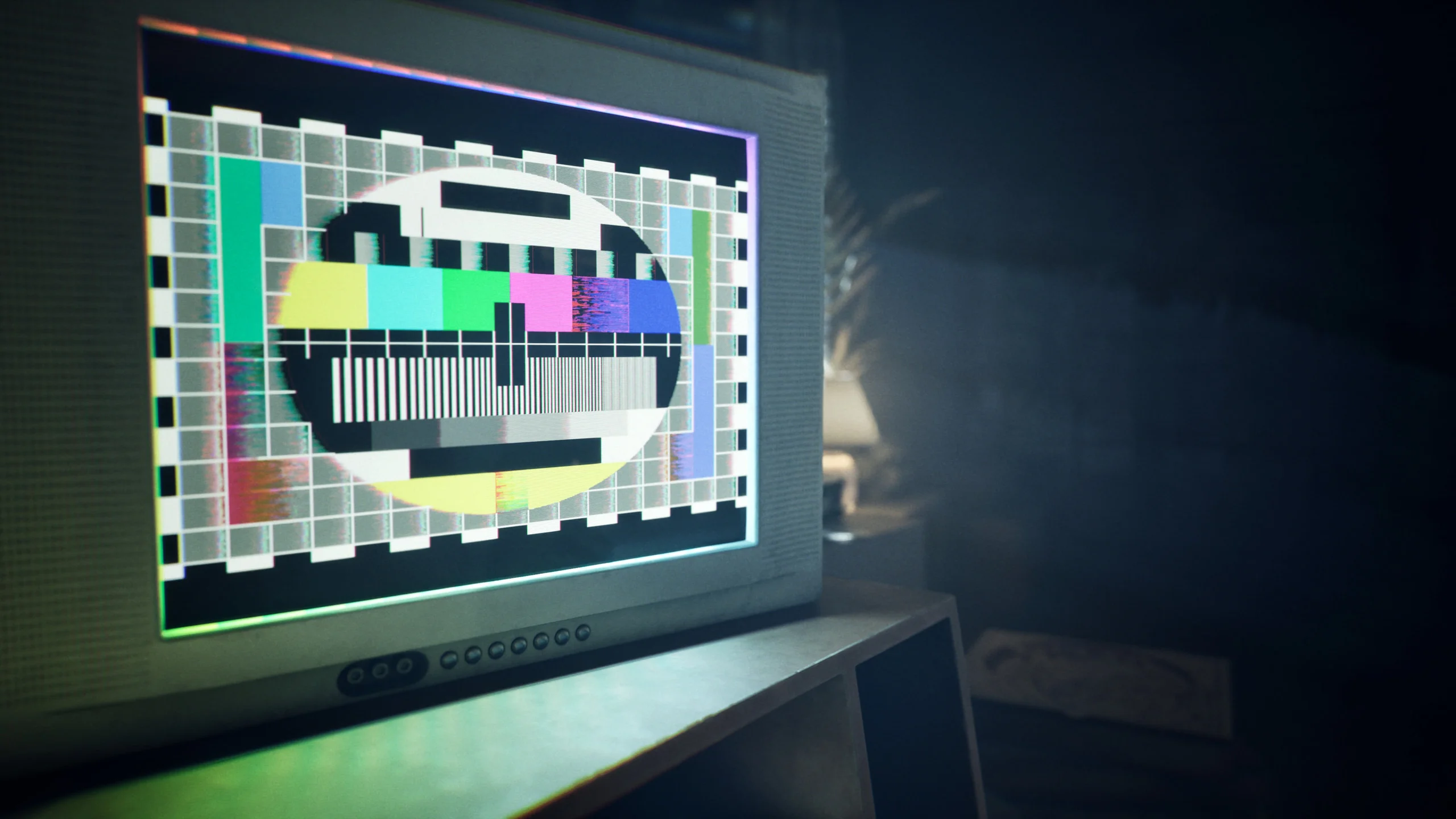 A CRT monitor glowing in a dark room, showing a glitching colour test card